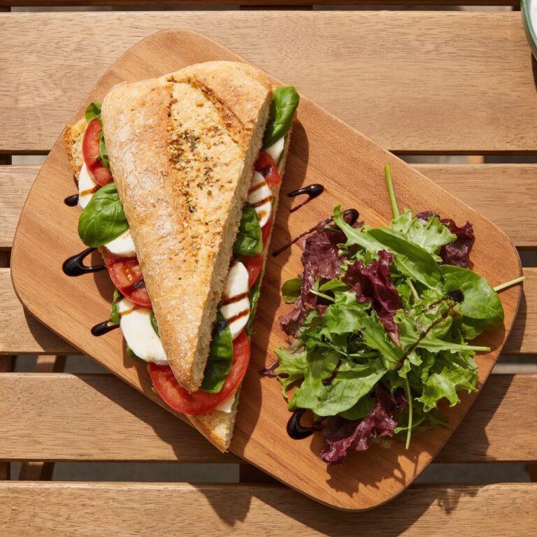 Caprese panini on a board with pressed ciabatta, mozzarella, tomato, basil, and balsamic glaze