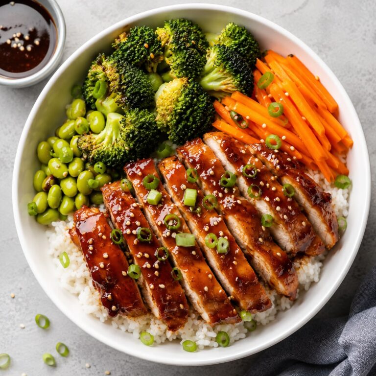 Glazed chicken teriyaki bowl with steamed rice, sautéed broccoli, carrots, and sesame seeds in a white bowl