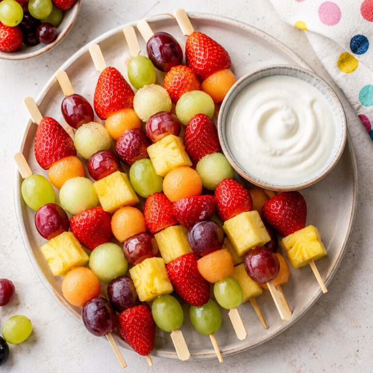 Colourful fruit skewers with strawberries, grapes, melon, and pineapple arranged with a bowl of creamy yogurt dip